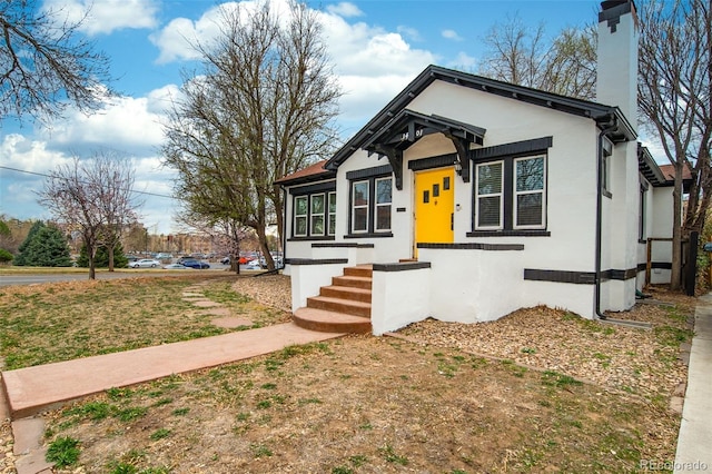 bungalow-style home with stucco siding and a chimney
