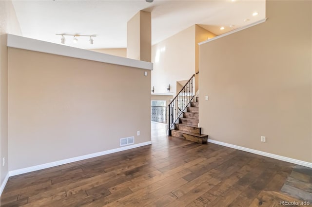 unfurnished living room with high vaulted ceiling, track lighting, and dark hardwood / wood-style flooring