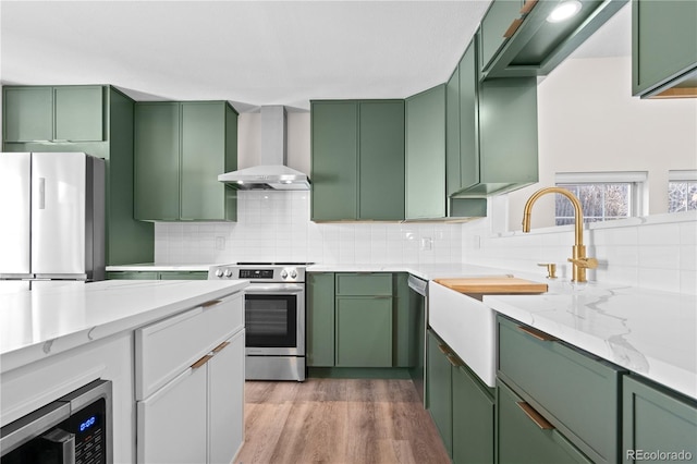 kitchen featuring appliances with stainless steel finishes, green cabinetry, and wall chimney exhaust hood