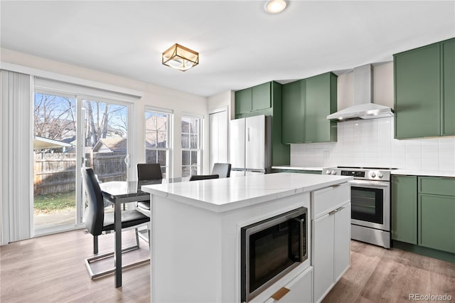 kitchen with backsplash, wall chimney exhaust hood, stainless steel appliances, light hardwood / wood-style flooring, and green cabinetry