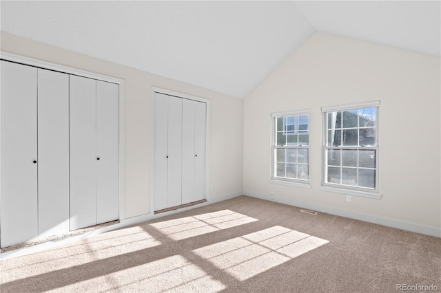 unfurnished bedroom with two closets, lofted ceiling, and light colored carpet