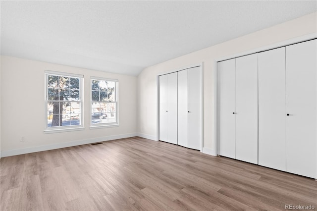 unfurnished bedroom featuring a textured ceiling, multiple closets, light hardwood / wood-style floors, and lofted ceiling