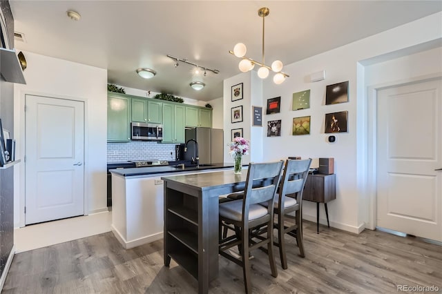 kitchen featuring appliances with stainless steel finishes, green cabinets, pendant lighting, light hardwood / wood-style floors, and backsplash