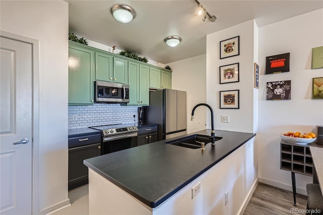 kitchen with sink, green cabinetry, kitchen peninsula, stainless steel appliances, and decorative backsplash