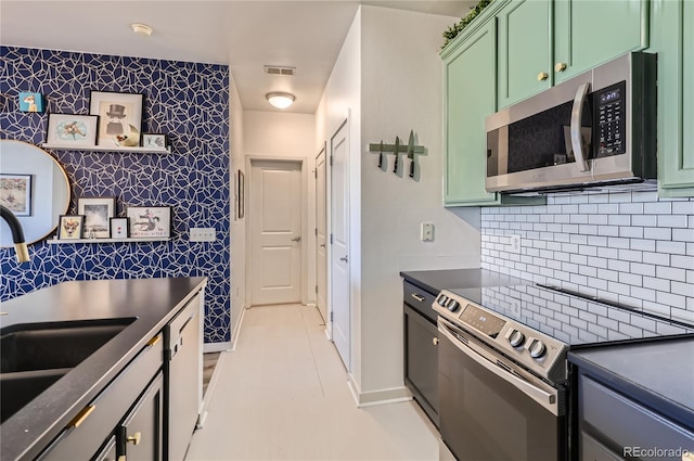 kitchen with stainless steel appliances, sink, green cabinets, and backsplash