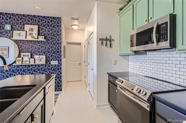 4100 Albion St Unit 221, Denver, CO 80216 - kitchen featuring appliances with stainless steel finishes, green cabinets, dark countertops, an accent wall, and wallpapered walls