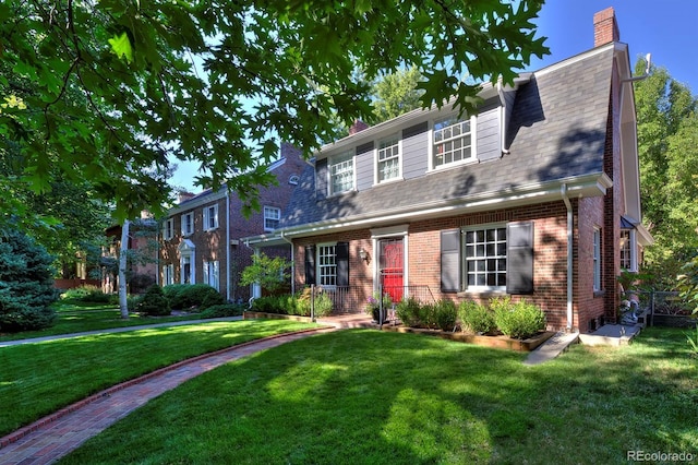 view of front of property featuring brick siding, roof with shingles, a front yard, and a chimney