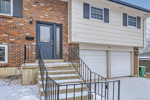 snow covered property entrance featuring a garage