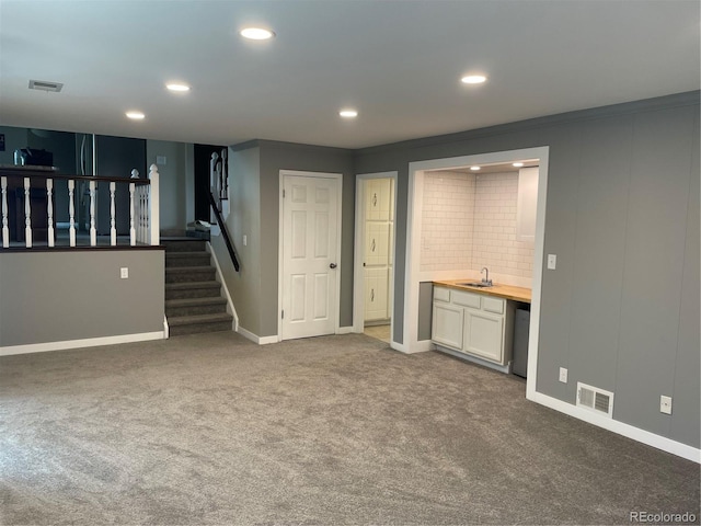 unfurnished living room with ornamental molding, dark colored carpet, and wet bar