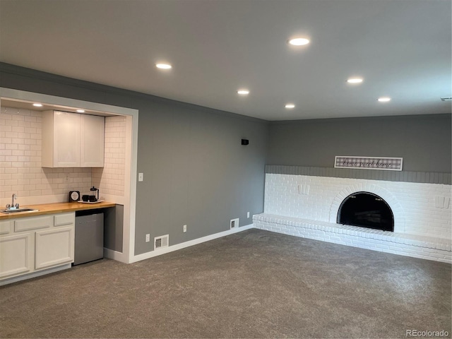 unfurnished living room featuring a brick fireplace, dark colored carpet, sink, and crown molding