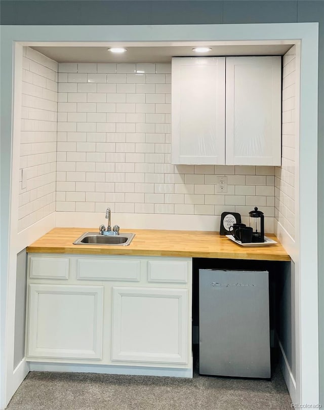 kitchen featuring white cabinets, stainless steel fridge, sink, tasteful backsplash, and wood counters