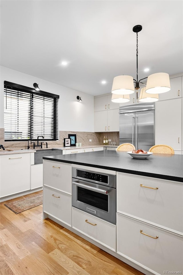 659 Albion St, Denver, CO 80220 - kitchen featuring appliances with stainless steel finishes, white cabinetry, dark countertops, light wood-type flooring, and tasteful backsplash