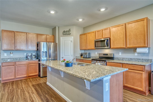 kitchen featuring stainless steel appliances, light wood-style floors, an island with sink, light stone countertops, and recessed lighting