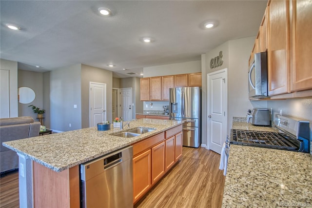 kitchen with appliances with stainless steel finishes, a sink, light wood-style flooring, a kitchen island with sink, and light stone countertops