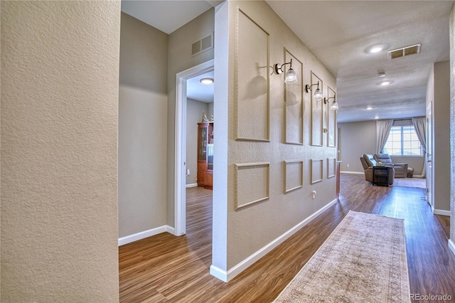 corridor with a textured wall, wood finished floors, and baseboards