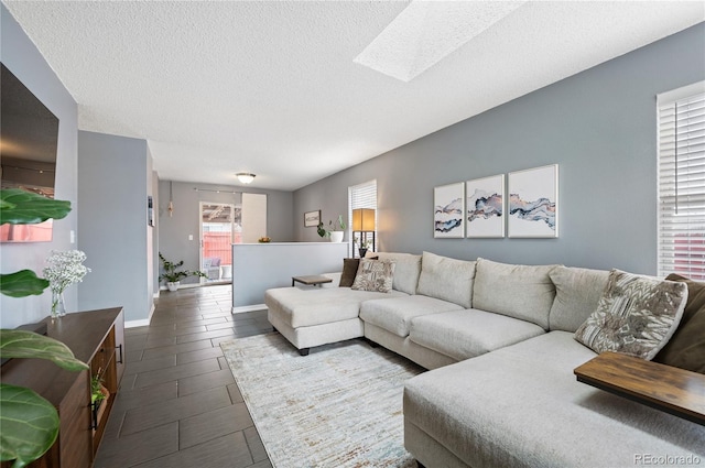 living room featuring a textured ceiling, wood finish floors, a skylight, and baseboards