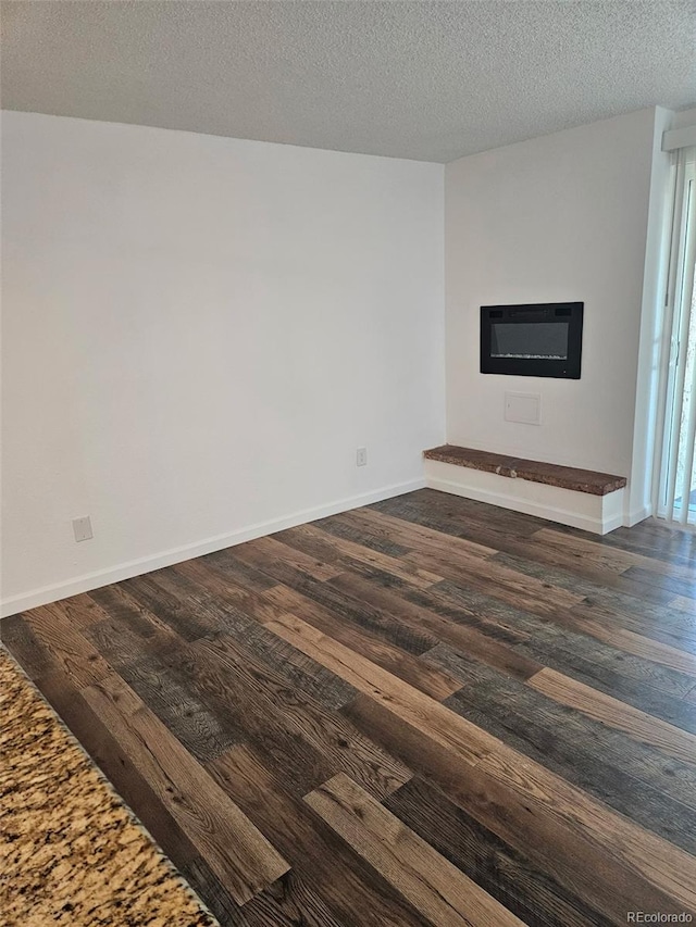 1304 S Parker Rd Unit 13, Denver, CO 80231 - empty room with dark wood-style floors, a glass covered fireplace, a textured ceiling, and baseboards