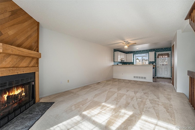 unfurnished living room featuring light carpet, a textured ceiling, and ceiling fan