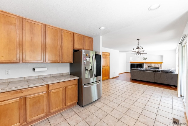 13180 Jasmine St, Thornton, CO 80602 - kitchen with stainless steel refrigerator with ice dispenser, tile countertops, a chandelier, light tile patterned floors, and open floor plan
