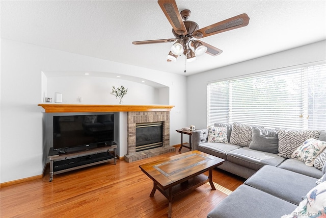 13180 Jasmine St, Thornton, CO 80602 - living room featuring a brick fireplace, wood finished floors, ceiling fan, baseboards, and a textured ceiling
