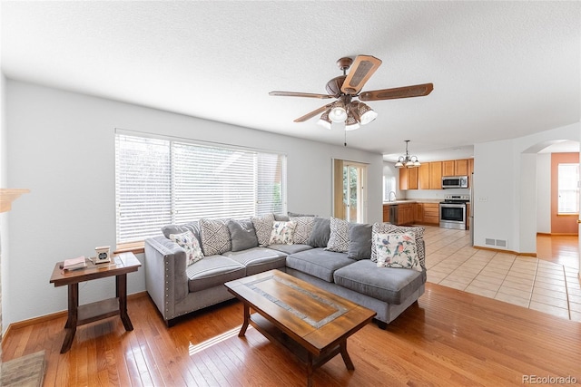 13180 Jasmine St, Thornton, CO 80602 - living room with arched walkways, a ceiling fan, healthy amount of natural light, light wood finished floors, and a textured ceiling