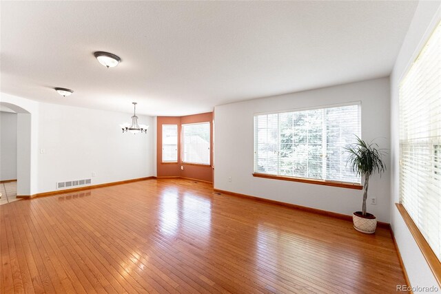 13180 Jasmine St, Thornton, CO 80602 - spare room featuring a chandelier, arched walkways, light wood-type flooring, and baseboards
