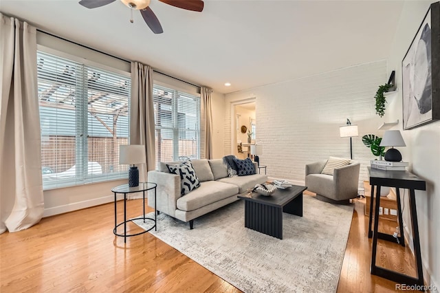 living area with baseboards, brick wall, ceiling fan, and light wood-type flooring