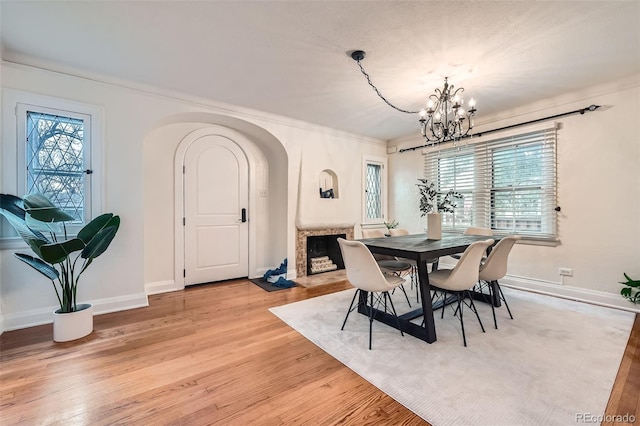 dining room with arched walkways, baseboards, light wood-style flooring, and a notable chandelier