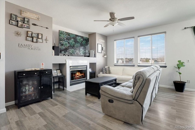 living area featuring a tiled fireplace, baseboards, ceiling fan, and wood finished floors