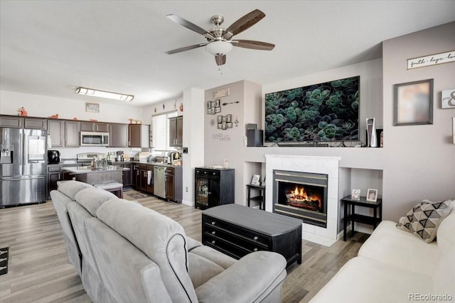 living area with a tiled fireplace, light wood finished floors, and ceiling fan