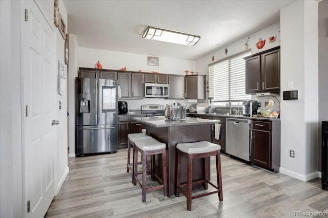 kitchen with dark brown cabinets, a kitchen island, a breakfast bar area, light wood-style floors, and stainless steel appliances