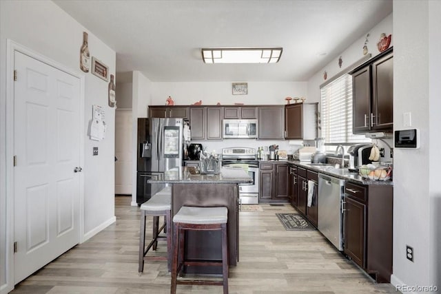 kitchen featuring a breakfast bar area, a sink, dark brown cabinetry, appliances with stainless steel finishes, and a center island