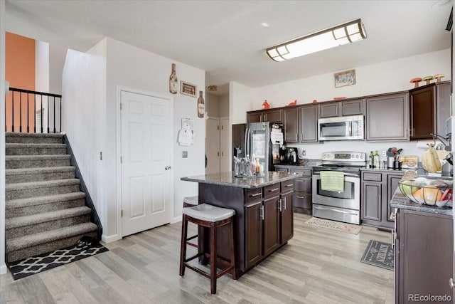 kitchen featuring a breakfast bar area, light wood-style flooring, dark brown cabinetry, appliances with stainless steel finishes, and a center island