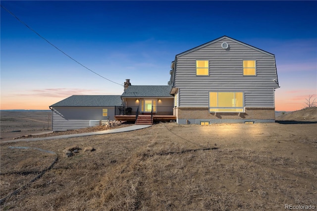 back of property at dusk featuring a deck, brick siding, and roof with shingles