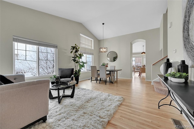 living room featuring arched walkways, high vaulted ceiling, visible vents, baseboards, and light wood-type flooring