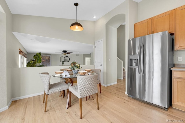 dining area featuring light wood-style floors, arched walkways, ceiling fan, and baseboards