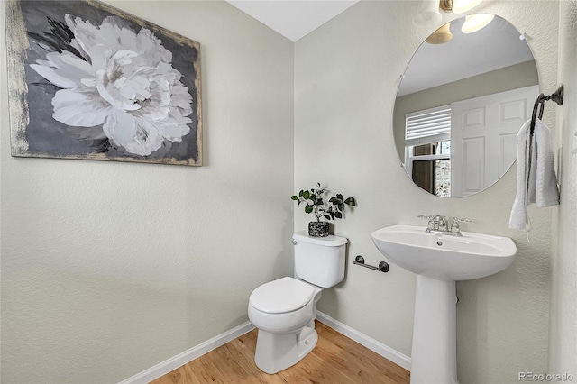 half bathroom with baseboards, a sink, toilet, and wood finished floors