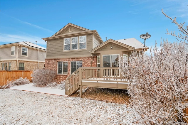 snow covered property with brick siding, fence, and a wooden deck