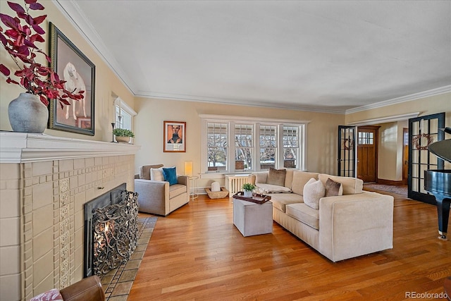 living room featuring a tiled fireplace, crown molding, radiator, and light hardwood / wood-style floors