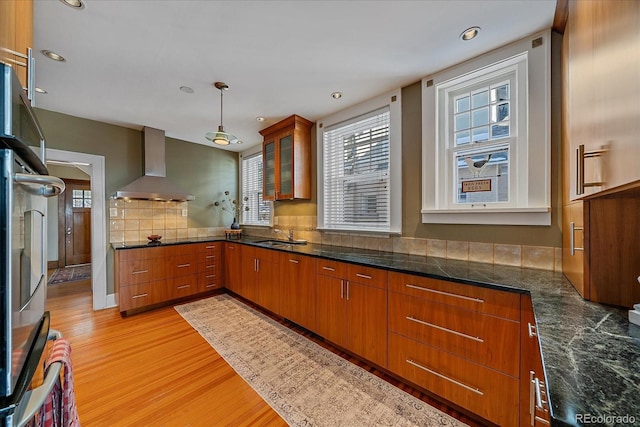 kitchen featuring wall chimney exhaust hood, sink, decorative light fixtures, light hardwood / wood-style flooring, and fridge