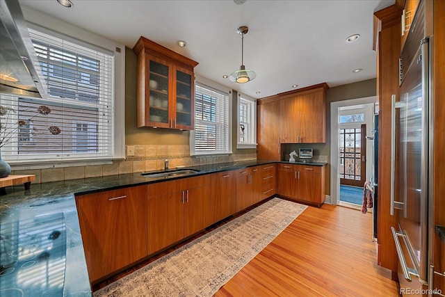 kitchen with pendant lighting, sink, built in refrigerator, dark stone countertops, and light wood-type flooring