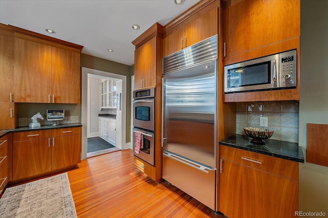 kitchen with appliances with stainless steel finishes, dark stone countertops, backsplash, and light wood-type flooring