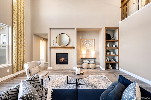 living room with a high ceiling, hardwood / wood-style flooring, and a tiled fireplace