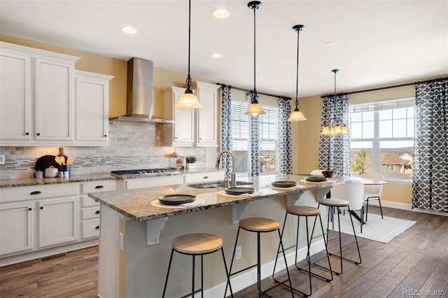 kitchen featuring an island with sink, decorative light fixtures, and wall chimney range hood