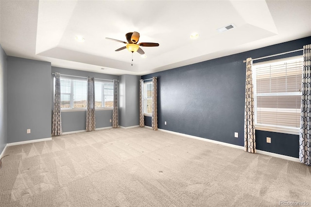 spare room with a raised ceiling, ceiling fan, and light carpet