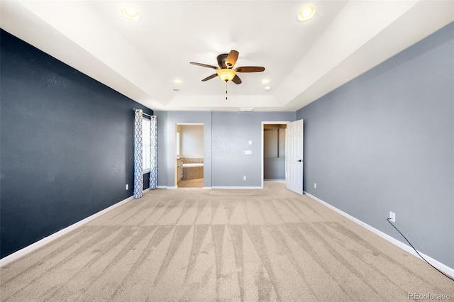 interior space featuring a raised ceiling, ensuite bathroom, ceiling fan, and light colored carpet