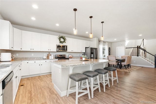 kitchen featuring appliances with stainless steel finishes, decorative light fixtures, light hardwood / wood-style flooring, a center island, and white cabinets