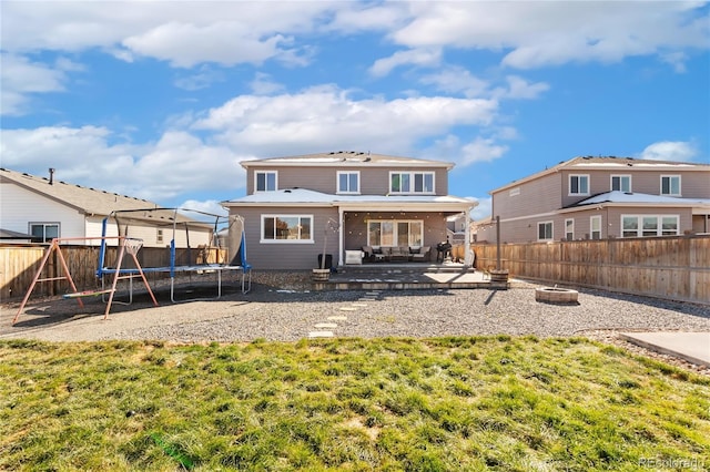 rear view of house with a fire pit, a trampoline, a patio, and a yard