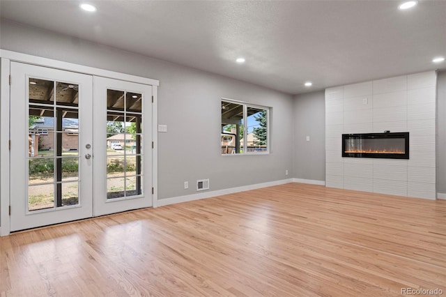 unfurnished living room with a tile fireplace, light hardwood / wood-style flooring, and french doors