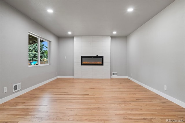 unfurnished living room with a tiled fireplace and light hardwood / wood-style flooring